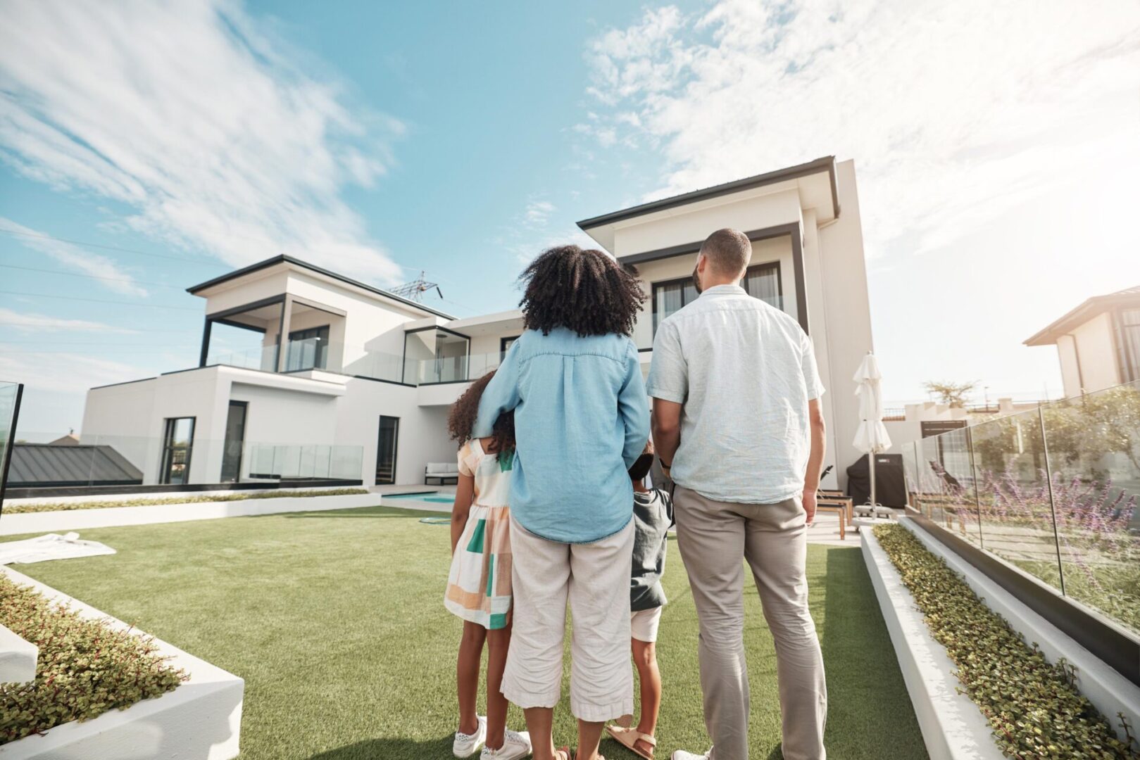 A family stands together, facing a modern two-story house with a lawn in the foreground.